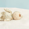 The Olli Ella Dozy Dinkum - Pickle Blossom, a soft cloth doll dressed in floral pajamas and a matching cap, lies on a white fuzzy surface against a light blue background, appearing to be peacefully sleeping.
