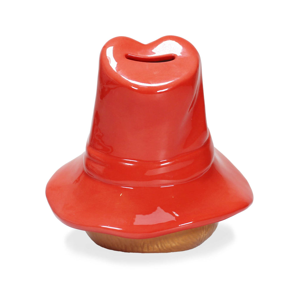The Paddington Money Bank is a ceramic coin bank featuring an oversized red cowboy hat with a coin slot on top and a brown base, perfect for fans to save up in style.