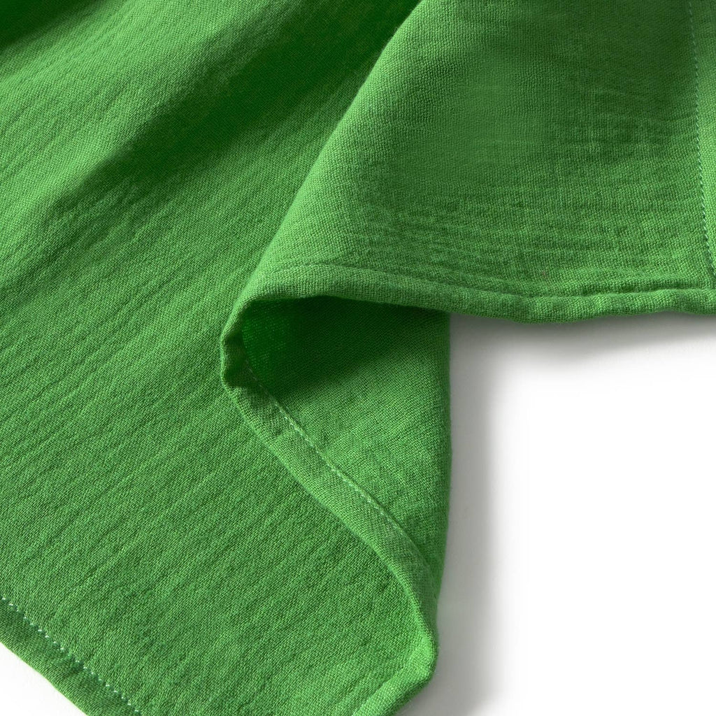 A close-up of Sweetie the Strawberry Big Doudou’s green organic cotton fabric, highlighting its texture and stitched hem, with a portion folded over on a white background.