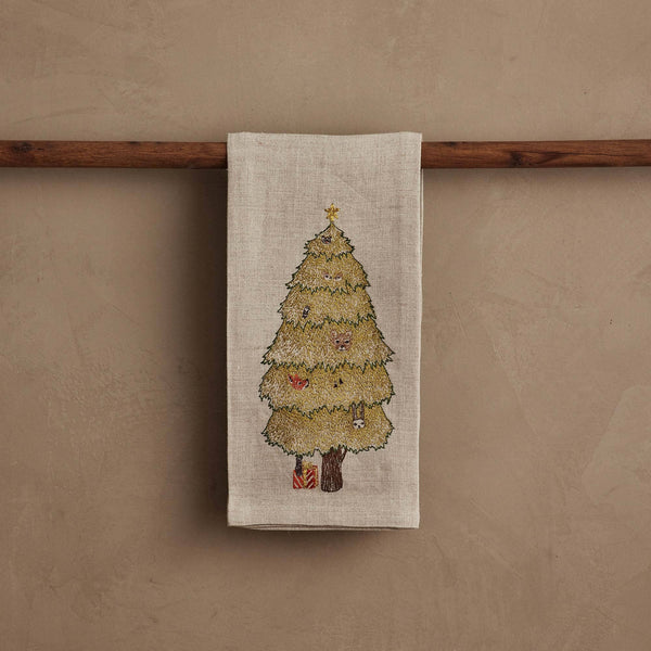 The Coral & Tusk Peek a Tree Tea Towel, in beige linen, hangs on a wooden rod and features an embroidered woodland Christmas tree with ornaments, a shining star, and tiny wrapped gifts—an ideal touch of holiday cheer.