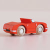 A No. 13 GT75 Marc, a small racing red wooden convertible with light wooden wheels, sits on a smooth, light-colored surface. Made in England, this car features simple painted details and a sleek, modern design that evokes the charm of a classic toy.