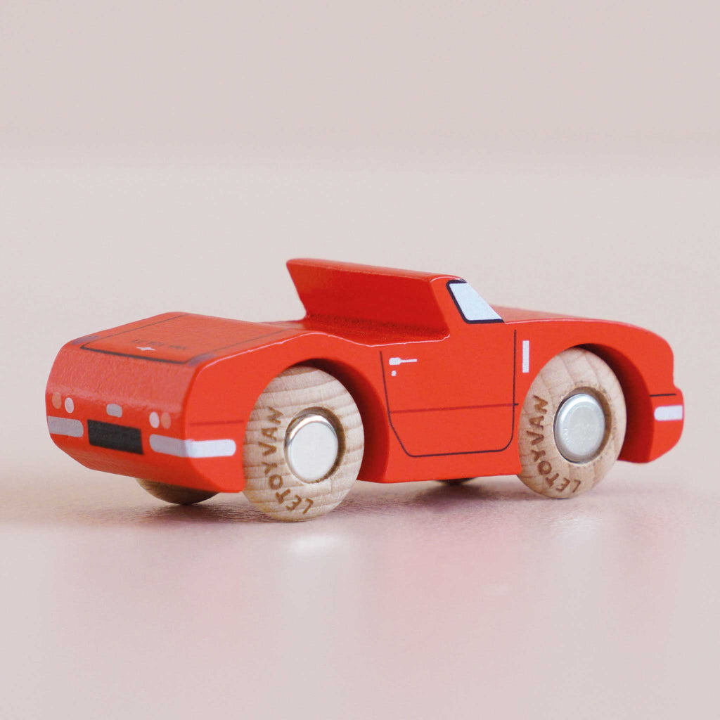 A No. 13 GT75 Marc, a small racing red wooden convertible with light wooden wheels, sits on a smooth, light-colored surface. Made in England, this car features simple painted details and a sleek, modern design that evokes the charm of a classic toy.