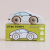 A classic toy car, the No. 16 GT90 Poppy, crafted from white wood with wooden wheels, sits atop a green box labeled “No. 16 GT90 Poppy.” The box displays an illustration of the wooden sports car along with icons indicating sustainable wood, made in United Kingdom, and child-safe paint.
