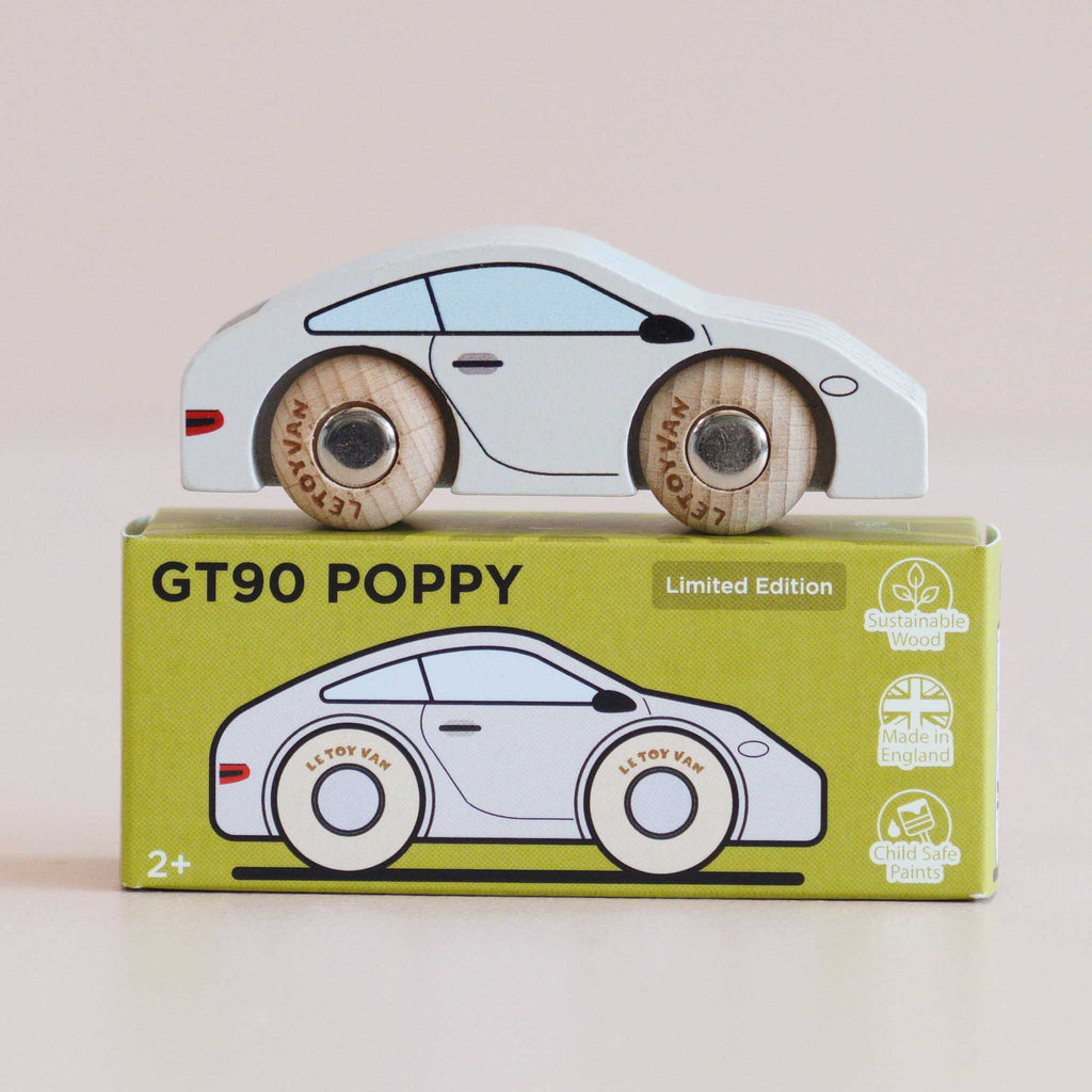 A classic toy car, the No. 16 GT90 Poppy, crafted from white wood with wooden wheels, sits atop a green box labeled “No. 16 GT90 Poppy.” The box displays an illustration of the wooden sports car along with icons indicating sustainable wood, made in United Kingdom, and child-safe paint.