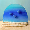 The Bumbu Handmade Wooden Deep Ocean Water Set includes three blue hand-shaped forms rising from wave-like bases, a gradient blue semicircle background, and wavy beige sand pieces, perfect for imaginative play and display.