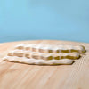 Three pieces from the Bumbu Handmade Wooden Deep Ocean Water Set, with wavy surfaces, rest on light wood against a soft blue background—ideal for imaginative play or stylish display.