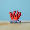 A small red coral figurine from the Bumbu Handmade Wooden Deep Ocean Water Set stands on a painted gray base against a light blue background and wooden surface, crafted from sustainable wood.
