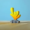 A small yellow and orange coral figurine from the Bumbu Handmade Wooden Deep Ocean Water Set, crafted from sustainable wood with a gray base, stands on a light wooden surface against a blue background.