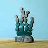 From the Bumbu Handmade Wooden Deep Ocean Water Set, this green seaweed-shaped wooden piece stands upright on a rounded gray base, inviting imaginative play against a serene light blue backdrop.