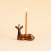 The Deer Cake Topper - Final Sale (ships in one week) is a handcrafted brown ceramic deer with gold accents, wearing a blue party hat and holding a lit taper candle on its back.