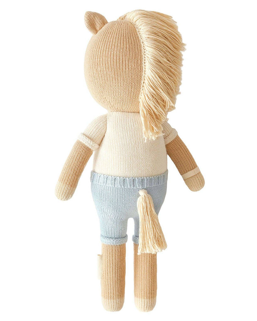Cuddle + Kind Liam the Pony is a hand-knit doll with a beige body, cream mane and tail, light blue pants, handmade in Peru, shown from the back.