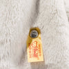 Close-up of a yellow Steiff tag and metal button attached to soft, light gray plush fabric, showing the Steiff Hoppie Bunny Stuffed Animal is handmade by Steiff.