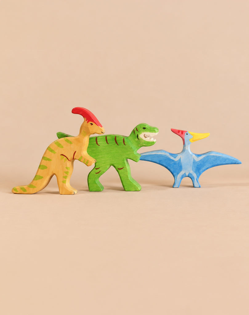 Holztiger Handmade Wooden Dinosaur Set featuring three figures for imaginative play: a yellow parasaurolophus, a green tyrannosaurus, and a blue pterosaur.