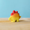 A colorful wooden Handmade Stegosaurus Baby Dinosaur toy, painted in gradients of yellow, orange, and red with non-toxic paint, stands on a wooden surface against a light blue background.