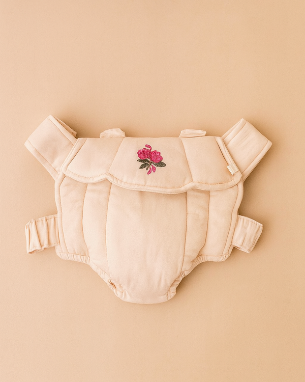 The Konges Sloejd Doll Carrier - Cameo Rose is a beige cotton carrier with padded straps and pink flower embroidery on the front, shown against a matching beige background.