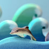 The Bumbu Handmade Wooden Dolphin Family Set features handcrafted dolphins nestled among painted blue and green waves, creating an eco-friendly ocean scene.