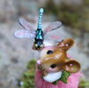 A close-up of the Wee Forest Folk Tiny Collectible—Pretty Perch in Pink (Not a Toy)—showcases a hand-sculpted mouse with a pink flower and a detailed blue dragonfly perched on its head, set against a softly blurred background.