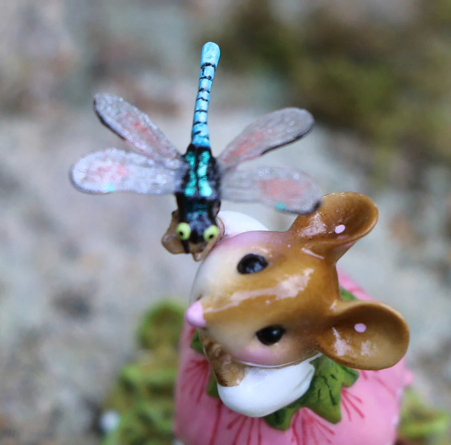 A close-up of the Wee Forest Folk Tiny Collectible—Pretty Perch in Pink (Not a Toy)—showcases a hand-sculpted mouse with a pink flower and a detailed blue dragonfly perched on its head, set against a softly blurred background.