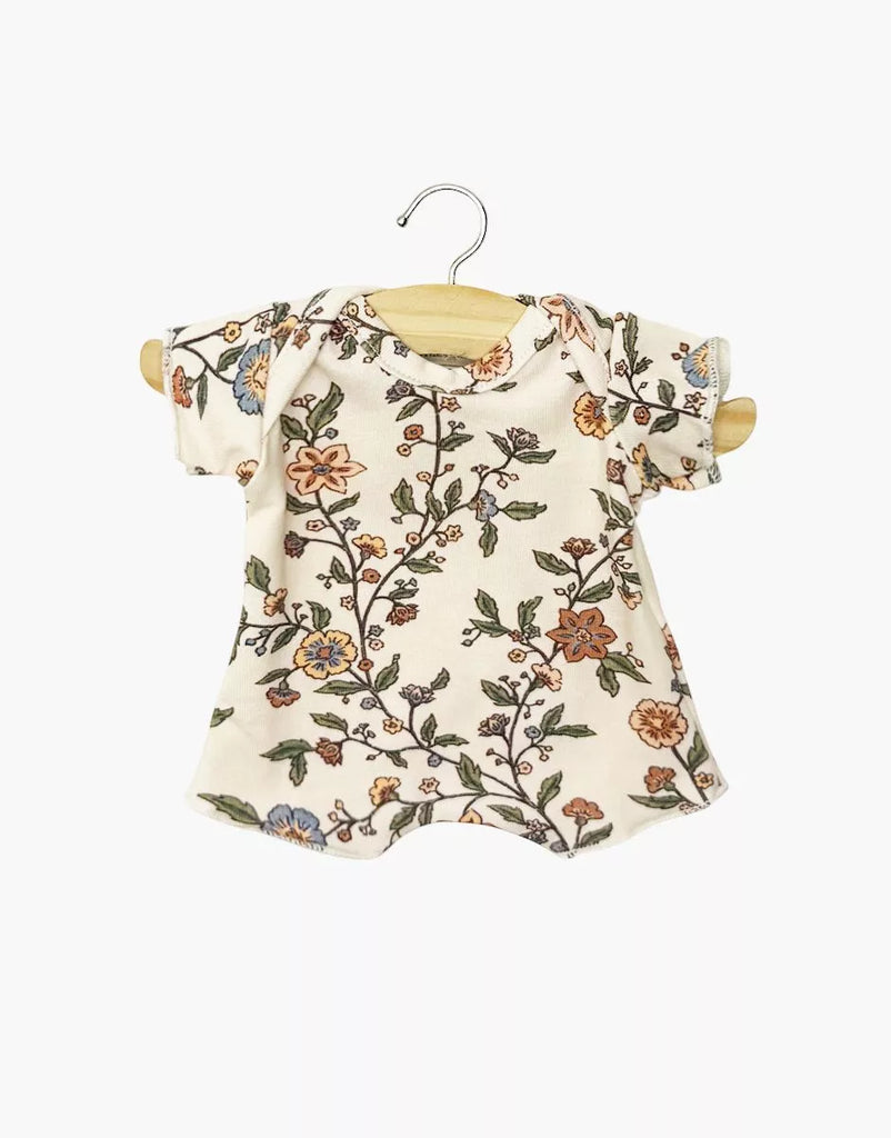 A Minikane 11" Doll Shorty Bodysuit in soft jersey, Gisele print, with short sleeves and a colorful floral pattern, hangs on a wooden hanger against a white background.