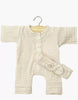 The Minikane 11″ Doll Clothing set features the Lili Jumpsuit & Headband in Cotton Gauze - Ecru: a cream-colored, long-sleeve romper with front buttons and a matching bow headband, crafted in France. Displayed on a wooden hanger, this charming set is perfect for dressing your Minikane doll and is photographed against a plain white background.