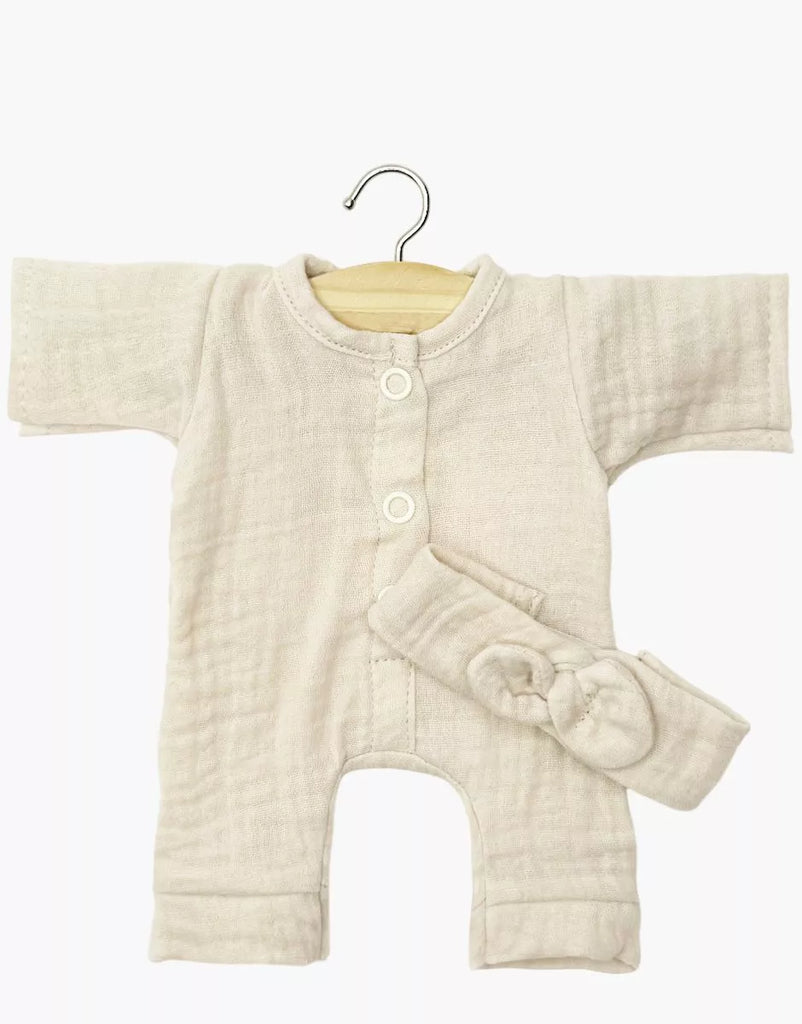 The Minikane 11″ Doll Clothing set features the Lili Jumpsuit & Headband in Cotton Gauze - Ecru: a cream-colored, long-sleeve romper with front buttons and a matching bow headband, crafted in France. Displayed on a wooden hanger, this charming set is perfect for dressing your Minikane doll and is photographed against a plain white background.