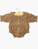 The Minikane Doll Clothing | Leonore Ruffled Romper in Crepe - Eloise features a brown crepe fabric, small floral print, long sleeves, wooden buttons, and ruffled collar and cuffs. Made in France for Gordis dolls; shown on a wooden hanger against a white background.