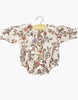 The Minikane 13" Doll Clothing | Leonore Ruffled Romper in Cotton Gauze - Gisele features a floral print in shades of pink, red, green, and purple, designed for 13 inch dolls and shown on a wooden hanger against a white background.