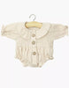 The Minikane 13" Doll Clothing | Leonore Ruffled Romper in Cotton Gauze - Putty features a cream-colored romper with long sleeves, ruffled collar, and brown buttons, made in France for 13 inch dolls. Displayed on a hanger against a white background.