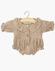 The Minikane Doll Clothing | Leonore Ruffled Romper in Cotton Gauze - Mocha is a mocha, long-sleeve romper with a Peter Pan collar and ruffled waist, designed for Minikane Gordis or 13" dolls, shown on a wooden hanger against a white background.