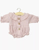The Minikane Doll Clothing | Leonore Ruffled Romper in Cotton Gauze - Orchid Pink features long sleeves, a ruffled collar, wooden buttons, gathered cuffs, and ruffled leg openings—perfect for 13 inch dolls like Minikane. Displayed on a wooden hanger.