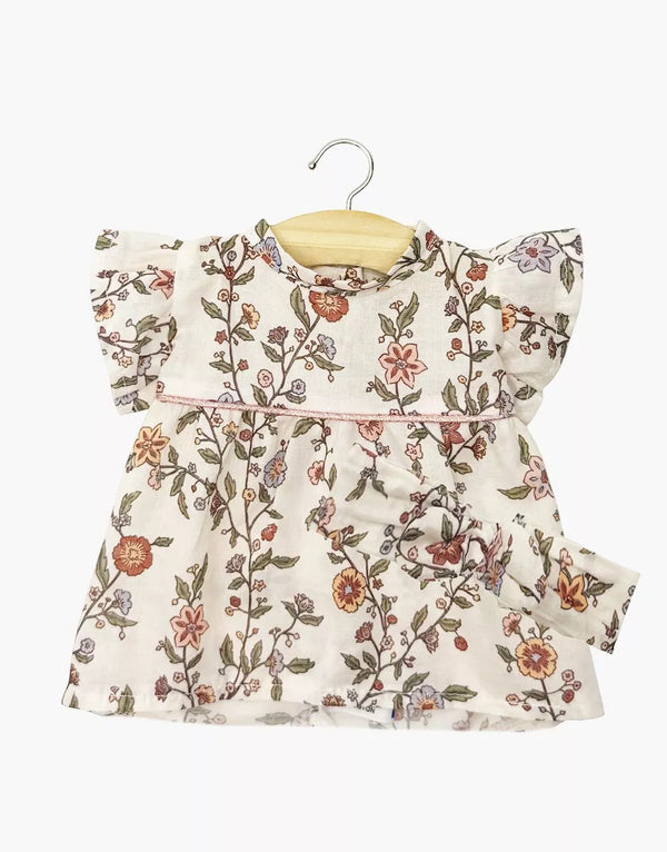 A cream cotton Daisy Dress with floral print, short ruffled sleeves, and matching headband for Minikane dolls. Displayed on a wooden hanger. Product: Minikane Doll Clothing | Daisy Dress & Headband in Cotton - Gisele.