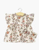A cream cotton Daisy Dress with floral print, short ruffled sleeves, and matching headband for Minikane dolls. Displayed on a wooden hanger. Product: Minikane Doll Clothing | Daisy Dress & Headband in Cotton - Gisele.