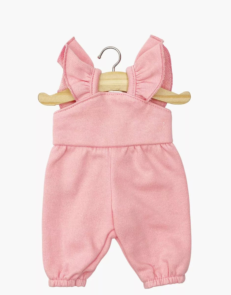 The Claudie Overalls in Cotton - Strawberry Pink for Minikane 13" dolls are displayed on a wooden hanger against a white background, featuring ruffled shoulder straps, an elastic waist, and leg openings. Perfect doll clothes for 13-inch dolls.