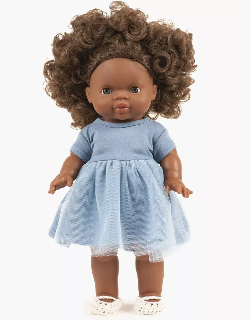 A curly-haired Minikane doll with brown skin wears the Rosana Short Sleeve Tutu in cobalt blue and white shoes, standing against a plain white background. Perfect for collectors of 14-inch dolls.