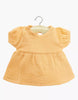 The Minikane 11" Doll Faustine Dress in Apricot is a small, short-sleeved outfit made of soft cotton gauze, shown on a wooden hanger against a white background.
