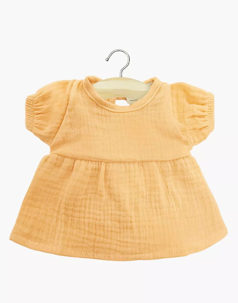 The Minikane 11" Doll Faustine Dress in Apricot is a small, short-sleeved outfit made of soft cotton gauze, shown on a wooden hanger against a white background.
