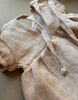A close-up of the Minikane 11" Doll Clothing Faustine Dress with balloon sleeves in nude linen, designed for Minikane Babies dolls, lying on a neutral surface.