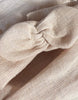 A close-up of nude washed linen fabric with a woven texture, folded and knotted—perfect for creating the Minikane Doll Clothing | Clara Romper & Headband in Washed Linen - Nude.