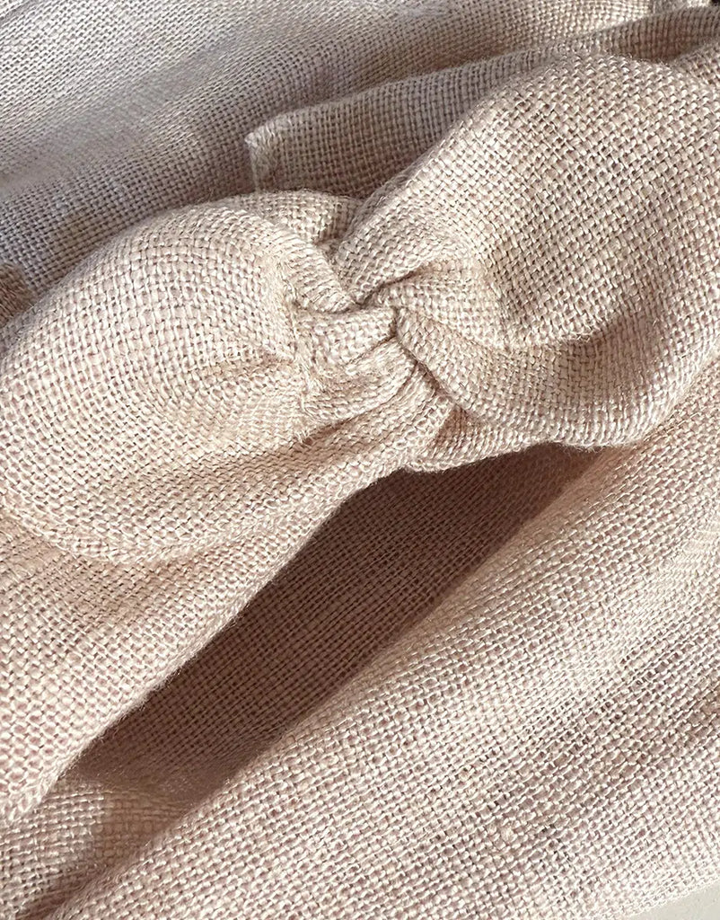 A close-up of nude washed linen fabric with a woven texture, folded and knotted—perfect for creating the Minikane Doll Clothing | Clara Romper & Headband in Washed Linen - Nude.