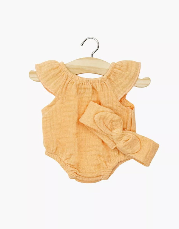 The Minikane Doll Clothing | Clara Romper & Headband in Cotton Gauze - Apricot features a peach romper with ruffled sleeves and a matching bow headband for Minikane Gordis dolls, shown on a wooden hanger against a white background.