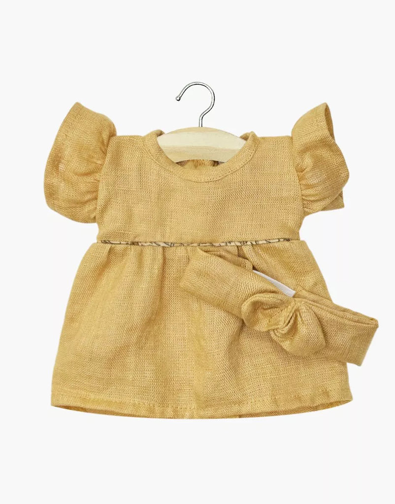A small, short-sleeved oatmeal Daisy dress with ruffled sleeves and a matching headband in washed linen for Minikane dolls, displayed on a wooden hanger against a plain white background.