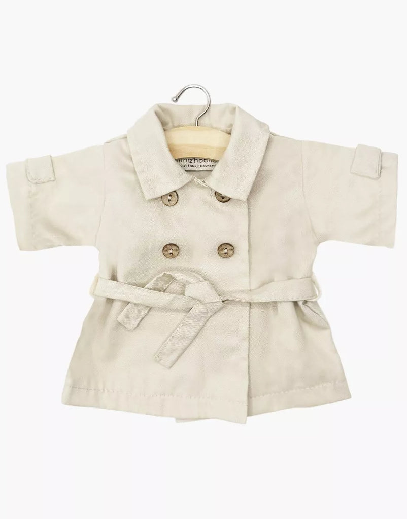 The Minikane Doll Clothing | Back to School - Tara Trench Coat in Beige Gabardine features double-breasted buttons, a tie belt, and rolled sleeves. Designed for 13" dolls, it's made in France and shown on a hanger against a white background.