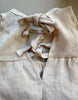 Close-up of the Minikane 13" Doll Sleeveless Faustine Dress in washed nude linen, made in France. Features two fabric ties knotted into bows for an open-back detail—perfect addition to a doll clothes collection.