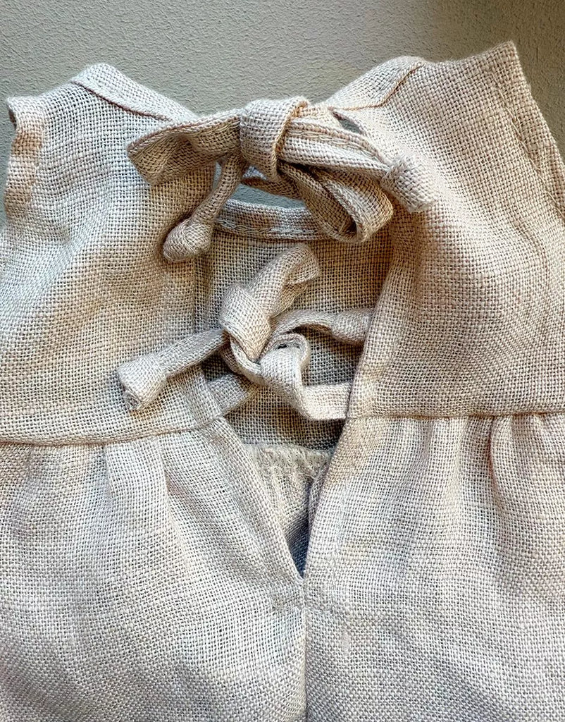 Close-up of the Minikane 13" Doll Sleeveless Faustine Dress in washed nude linen, made in France. Features two fabric ties knotted into bows for an open-back detail—perfect addition to a doll clothes collection.