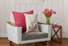 A gray armchair with a red cushion and an Easter Bunny Pocket Pillow sits beside a wooden side table holding pink tulips in a vase and a small white bowl, all set against a white paneled wall, creating an ideal decorative scene.