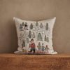 The Coral & Tusk Winter Fun Pillow features woodland animals in scarves and coats skiing, sledding, and walking among snowy trees—perfect holiday decor for your home. Shown on a wooden surface against a tan wall.
