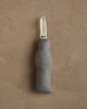 A gray fabric door draft stopper with a curved shape and white loop handle hangs on a textured beige wall—a cozy addition to homes featuring the Coral & Tusk Dog with Gifts Ornament.