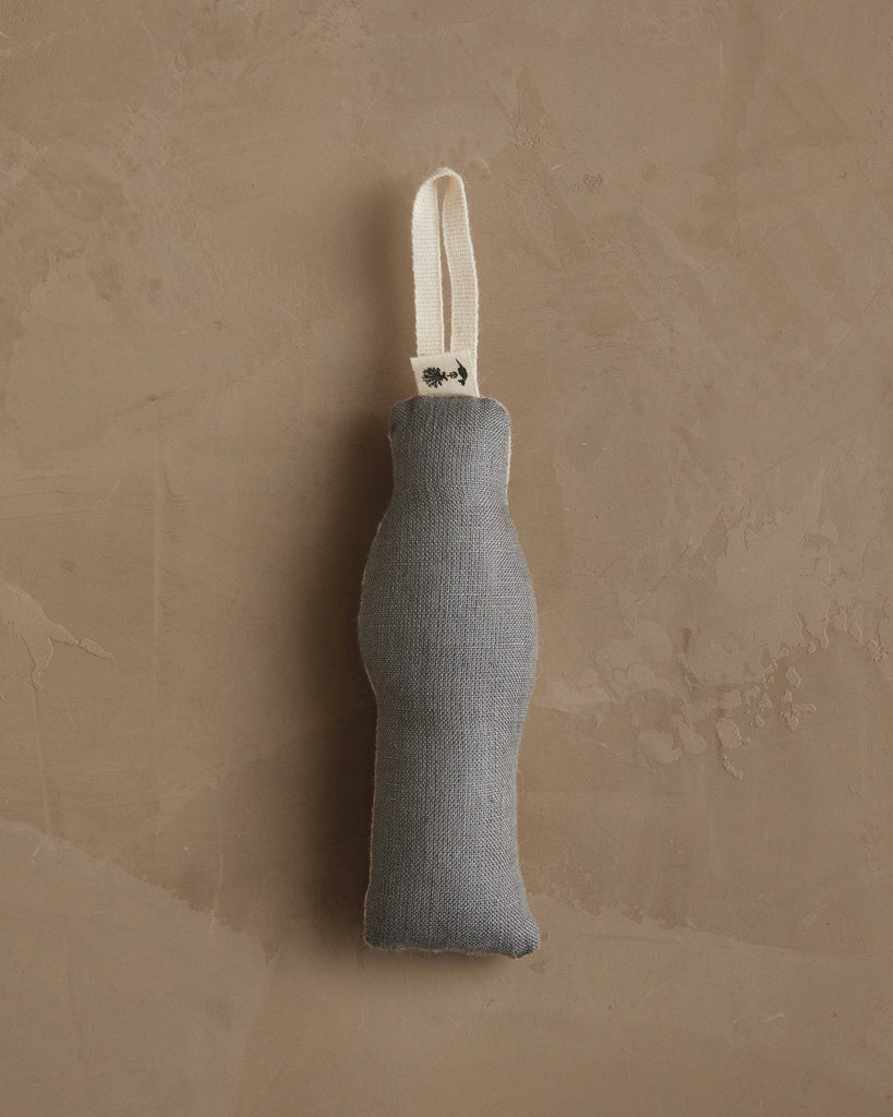 A gray fabric door draft stopper with a curved shape and white loop handle hangs on a textured beige wall—a cozy addition to homes featuring the Coral & Tusk Dog with Gifts Ornament.