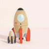 The Magnetic Space Rocket Duo features two wooden rockets, one with red fins and a window and the other with dark fins. Both are decorated with playful details, perfect for inspiring creative play on any light-colored surface.