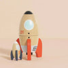 The Magnetic Space Rocket Duo features two wooden toy rockets with red fins and window details, standing upright on a light pink surface. Their playful, minimalist design is ideal for fans of plastic-free toys. Ships in one week.